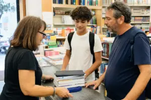 Commessa in libreria con genitore e studente al banco, accanto a una pila di libri di scuola e un tablet