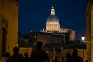 Cupola illuminata del santuario di Santa Rosa di notte, sopra i tetti del centro storico, con persone in silhouette in