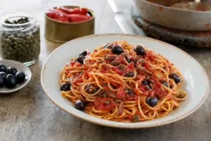 Spaghetti alla puttanesca in piatto rustico, con sugo di pomodoro, olive nere, capperi e acciughe