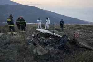 Rottami di un ultraleggero bruciato su un pendio roccioso, con soccorritori e nastro di sicurezza sullo sfondo