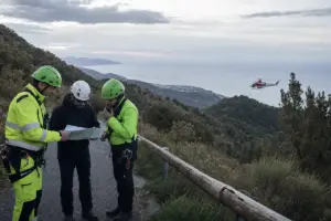 Soccorritori con caschi e giubbotti ad alta visibilità consultano una mappa su una strada in collina, con elicottero sullo