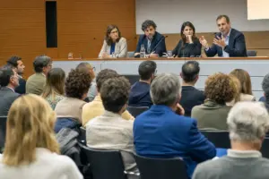 Panel in auditorium con relatori al tavolo e pubblico seduto che ascolta un intervento