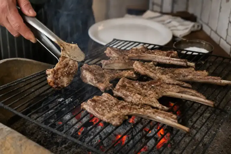 Costolette di abbacchio sulla griglia a carbonella, con sale e pepe, mentre una mano le gira con pinze