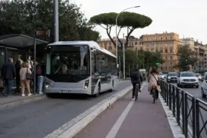 Autobus elettrico in fermata con pendolari e pista ciclabile protetta, traffico di auto sullo sfondo