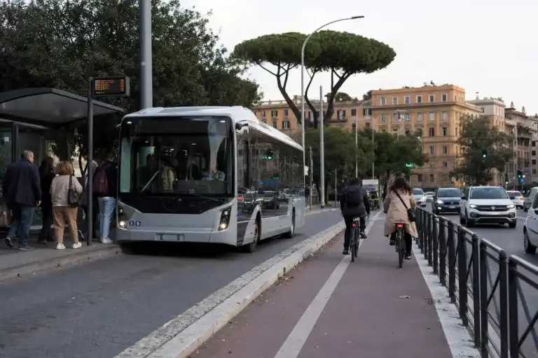 Autobus elettrico in fermata con pendolari e pista ciclabile protetta, traffico di auto sullo sfondo