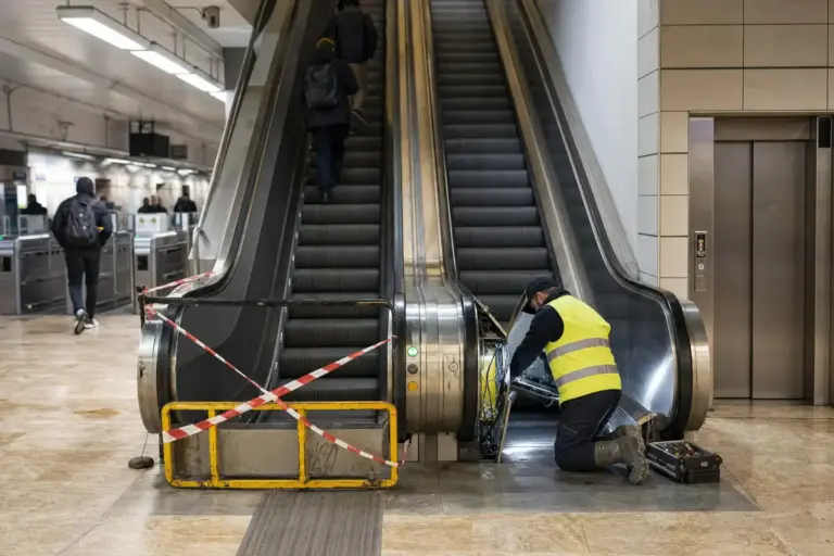 Tecnico al lavoro su una scala mobile in manutenzione in stazione metro, con ascensore e tornelli sullo sfondo