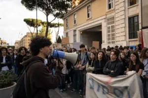 Studente con megafono parla davanti a un gruppo di giovani in presidio davanti a un edificio istituzionale